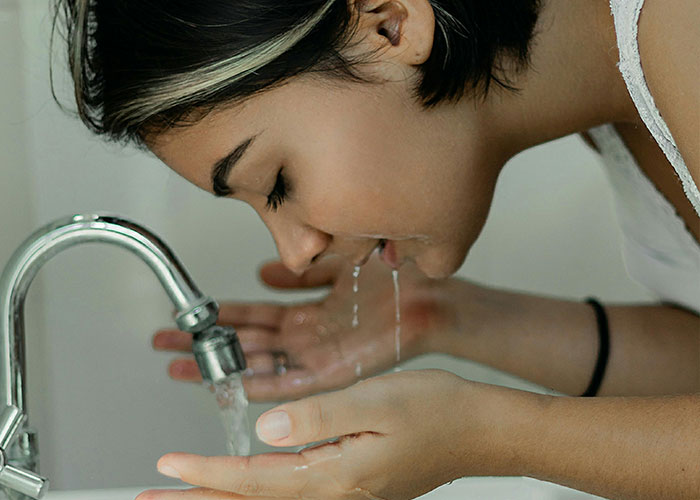 Woman washing her face at a sink, practicing beauty tips for skincare routine.