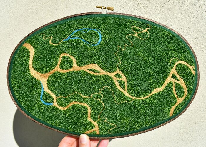 Hand holding a landscape embroidery piece featuring green textures and intricate patterns, embodying nature's beauty.