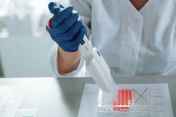 Person in a lab coat using a pipette with test samples, representing genetics research and data concerns. Person in a lab coat using a pipette with test samples, representing genetics research and data concerns.