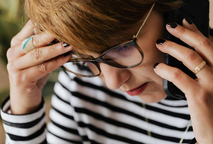 Person in glasses talking on the phone, appearing concerned, possibly discussing life-saving information.