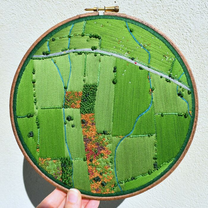 Landscape embroidery art featuring vibrant green fields in a circular hoop.