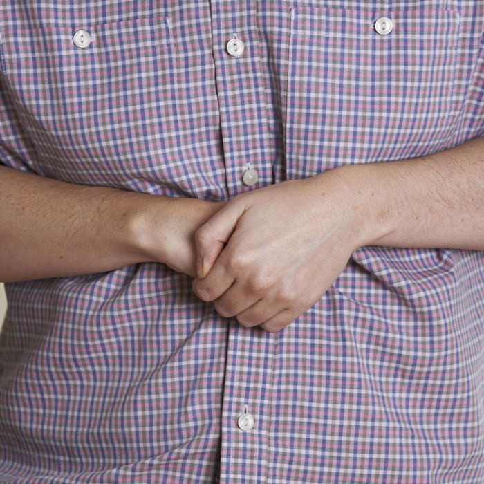 Person demonstrating a life-saving Heimlich maneuver technique, hands clasped over the abdomen, wearing a checked shirt.