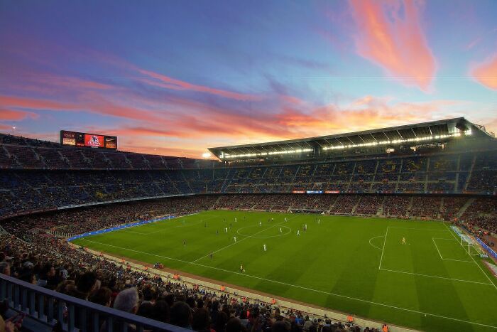 A large soccer cathedral stadium filled with fans watching a match under a colorful sunset sky.