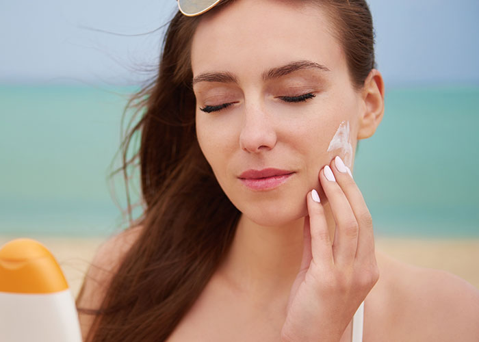 Woman applying sunscreen on the beach, highlighting essential beauty tips for skincare.