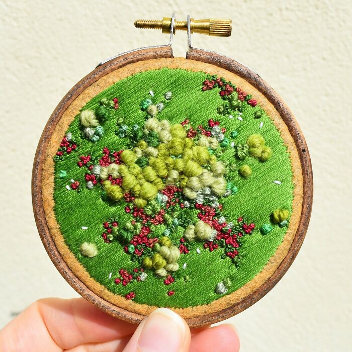 Embroidery art in a hoop showcasing intricate green and red landscape by Victoria Rose Richards.