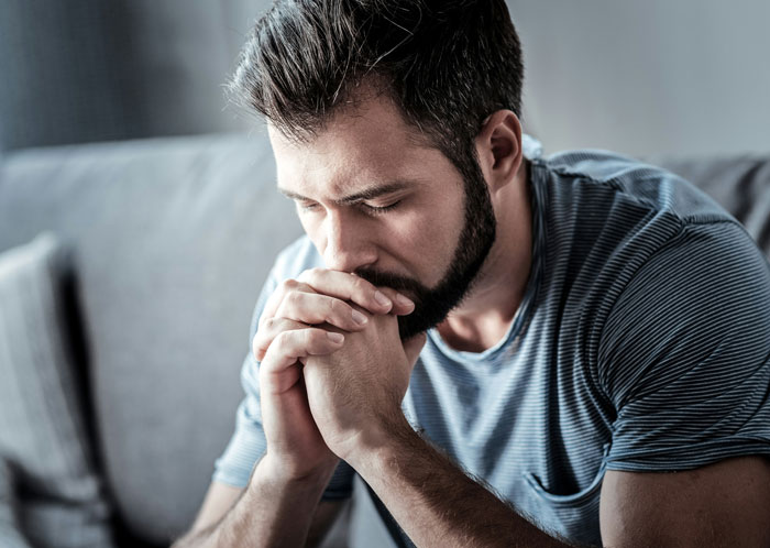 Man contemplating on a sofa, wearing a striped shirt, reflecting on relationship challenges. Man contemplating on a sofa, wearing a striped shirt, reflecting on relationship challenges.