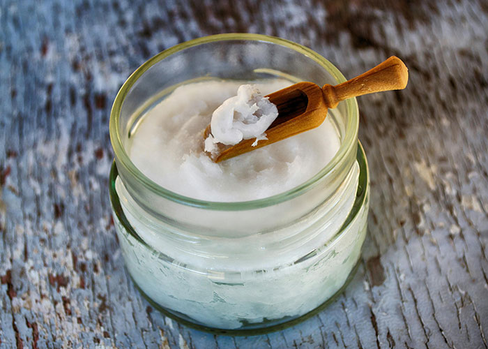 Glass jar of coconut oil with wooden spoon, highlighting beauty tips.