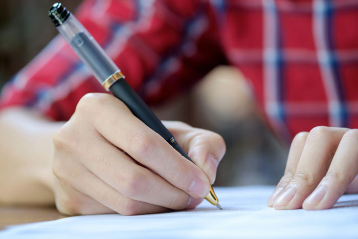 A person in a red plaid shirt writing with a fountain pen on paper, symbolizing inheriting a massive fortune. A person in a red plaid shirt writing with a fountain pen on paper, symbolizing inheriting a massive fortune.