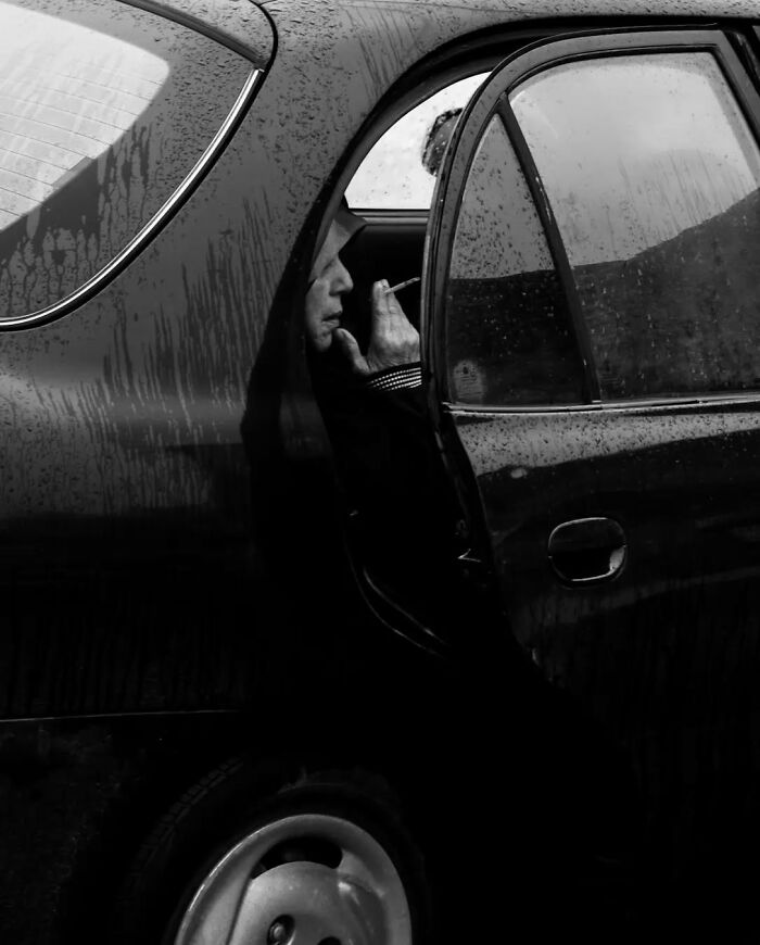Man smoking in the backseat of a car, showcasing raw street life beauty in a black and white photograph.
