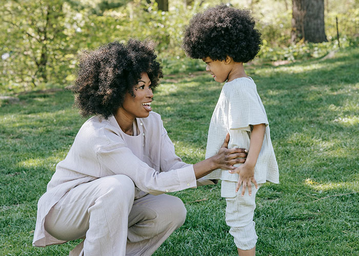Mom engaging in gentle parenting with her child in a sunny park, both smiling and wearing light outfits. Mom engaging in gentle parenting with her child in a sunny park, both smiling and wearing light outfits.