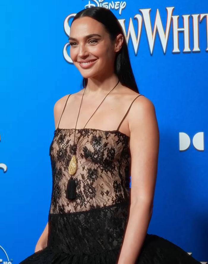 Actress in a black lace dress at a 'Snow White' event, smiling against a blue background. Actress in a black lace dress at a 'Snow White' event, smiling against a blue background.