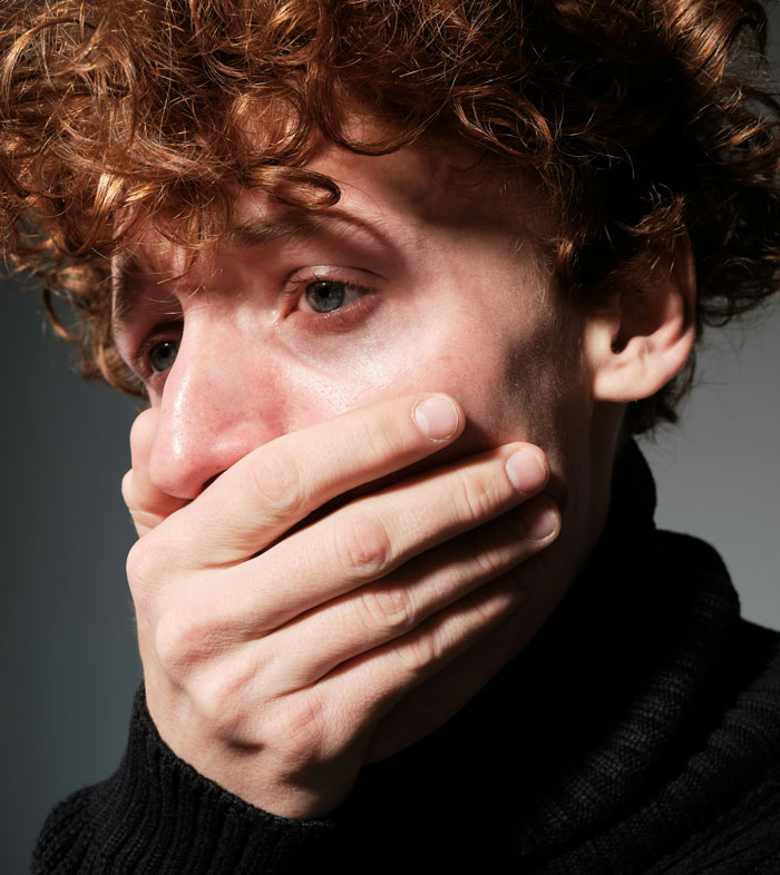 A person with red hair looks distressed, covering their mouth in a shadowed setting, related to breakup assumption and burn scars. A person with red hair looks distressed, covering their mouth in a shadowed setting, related to breakup assumption and burn scars.