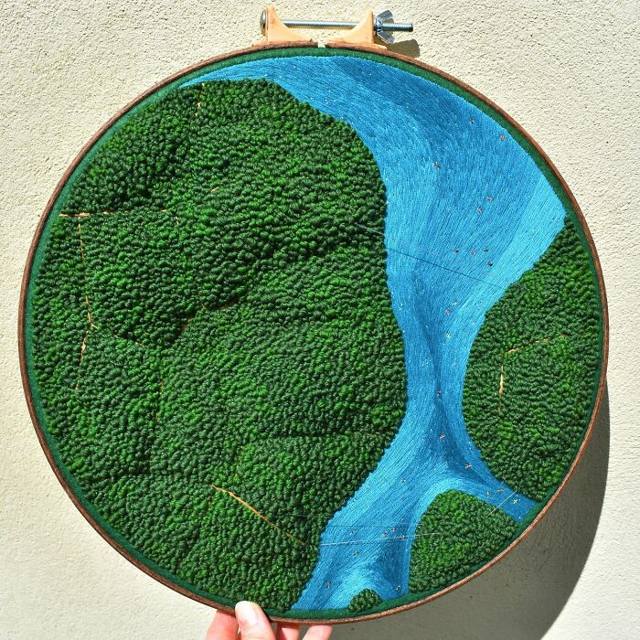 Landscape embroidery featuring a lush forest and winding river in a hoop.