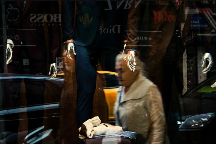 Street life captured with a blurred figure passing by a store window with mannequins and reflections of city activity.