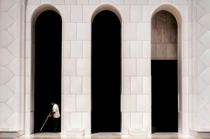 Photographer captures street life: person cleaning under arched doorways in a minimalist urban setting.