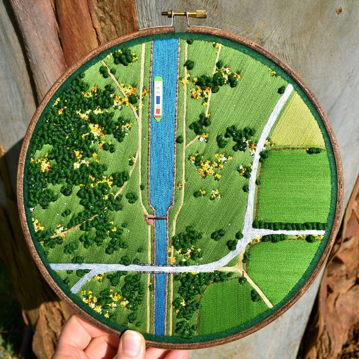 Landscape embroidery featuring vibrant fields and a river, crafted with intricate details.
