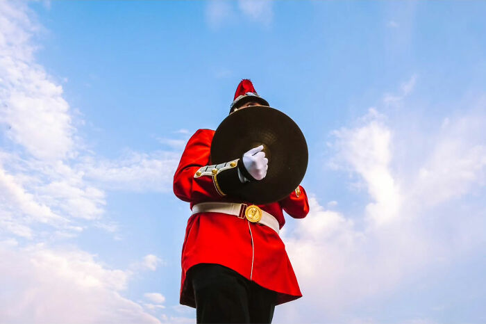Street life beauty captured in a photo of a marching band member in a red uniform, holding cymbals against a clear sky.