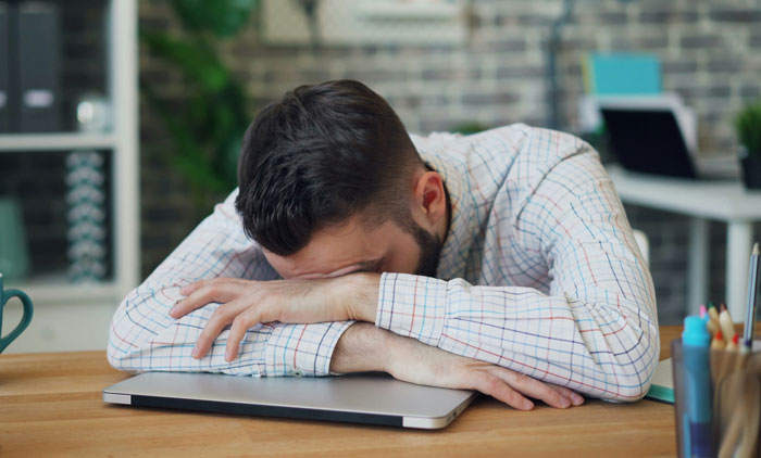 A frustrated man in a plaid shirt rests his head on a laptop, waiting for karma at work. A frustrated man in a plaid shirt rests his head on a laptop, waiting for karma at work.