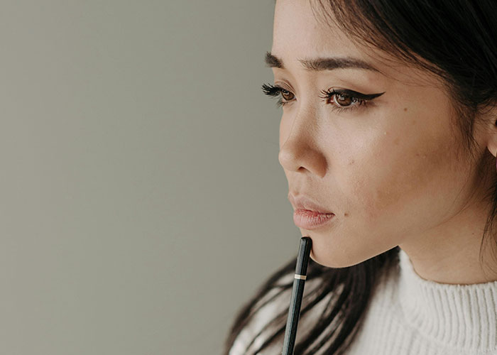 Woman in deep thought holding a pen, wearing a white sweater, contemplating property investment. Woman in deep thought holding a pen, wearing a white sweater, contemplating property investment.
