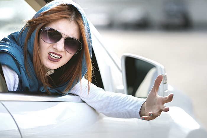 Woman in sunglasses gesturing from car window, looking frustrated. Woman in sunglasses gesturing from car window, looking frustrated.