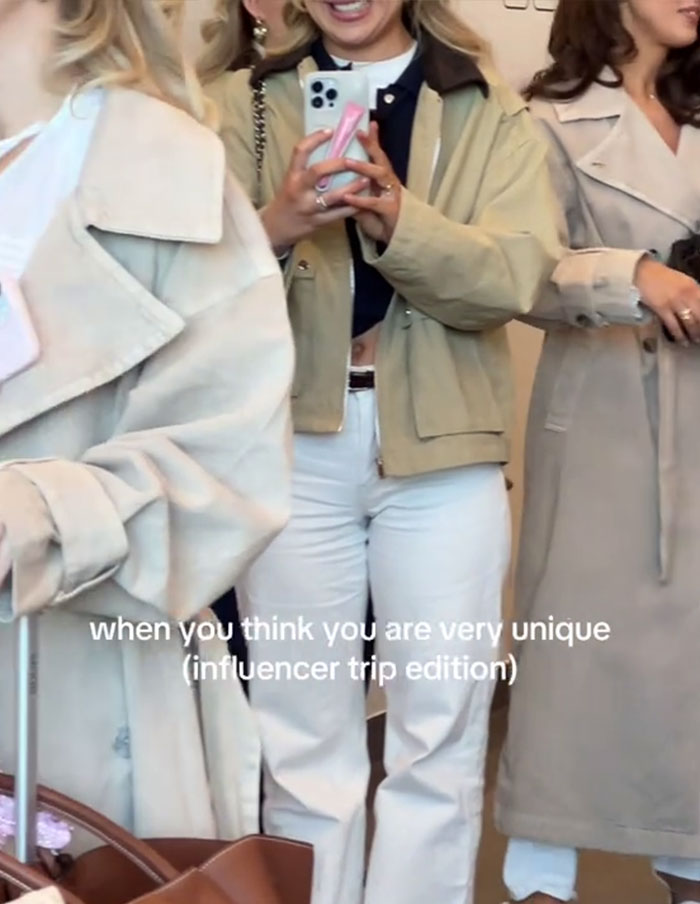 Influencers in similar beige trench coats at an event, reflecting a uniform fashion trend. Influencers in similar beige trench coats at an event, reflecting a uniform fashion trend.