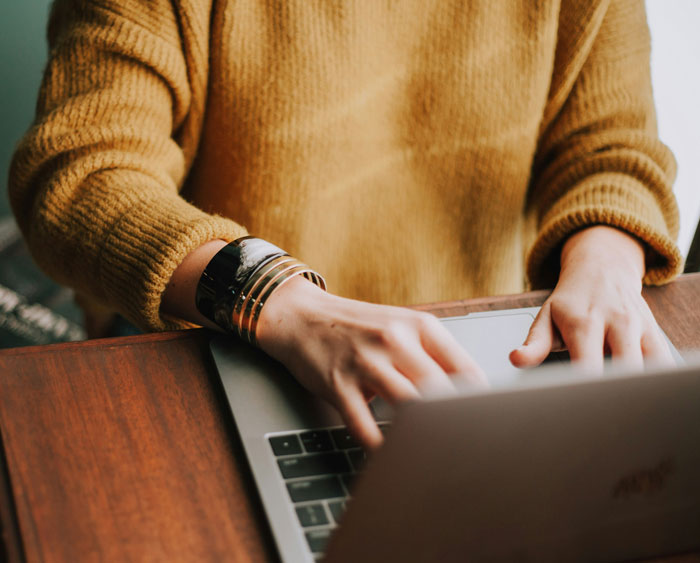 Person in a mustard sweater typing on a laptop, highlighting life-saving information resources online.