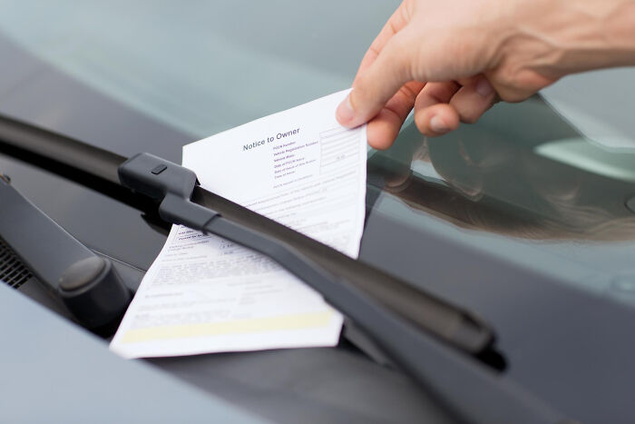 Hand placing a fake parking ticket under a windshield wiper for a fun April Fools' prank.