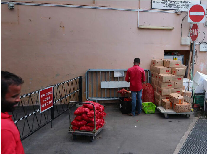 Street life scene with two men in red shirts organizing red bags and cardboard boxes near a "Keep Clear" sign.