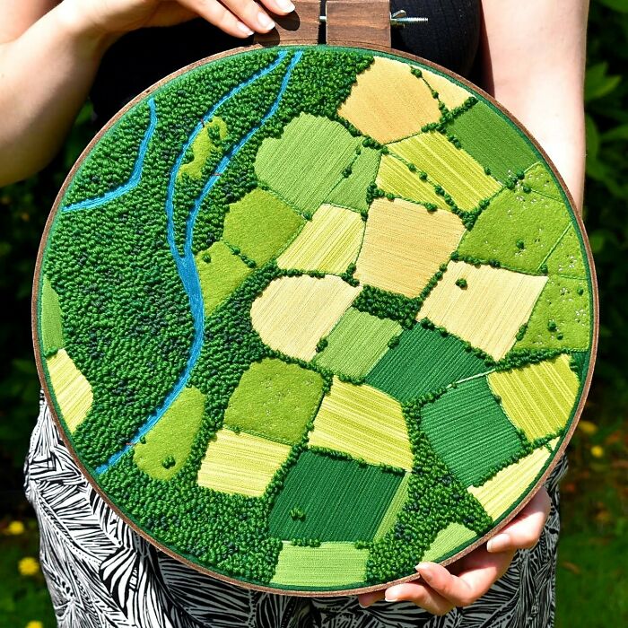 Landscape embroidery featuring green and yellow fields with a blue river, created by Victoria Rose Richards.