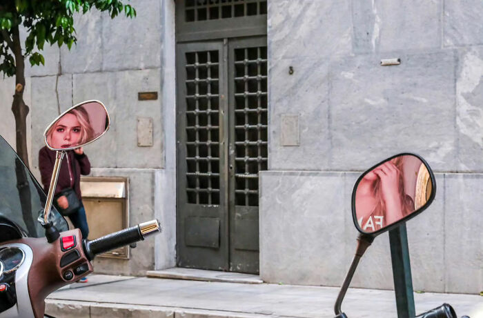 Street life captured in scooter mirrors, showing a woman's reflection in an urban setting.