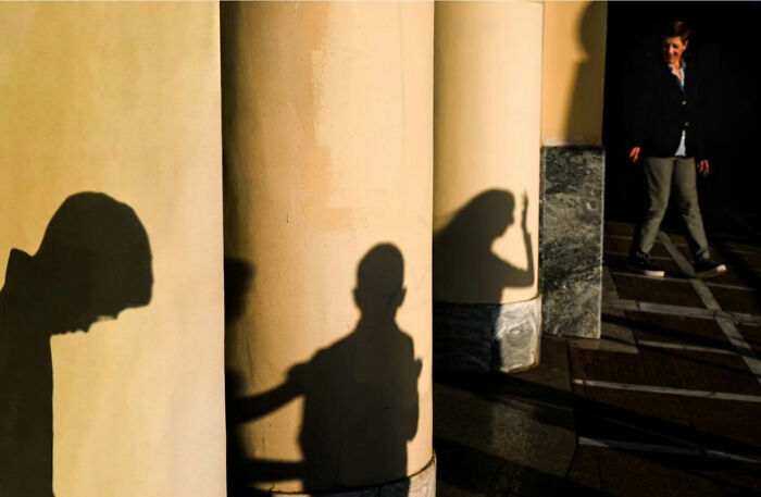 Shadows cast on columns with a person walking by, capturing street life's raw beauty.