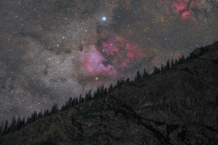Astrophotography capturing a vibrant night sky with colorful nebulae above a silhouetted mountain ridge.