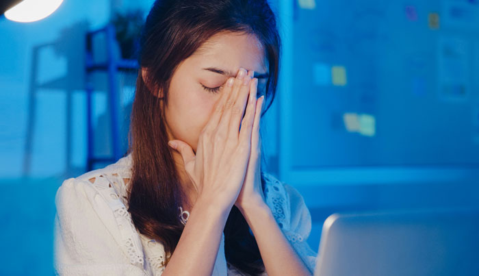 A woman looking stressed with eyes closed, hands on face, sitting in front of a laptop, referencing wedding explanation context. A woman looking stressed with eyes closed, hands on face, sitting in front of a laptop, referencing wedding explanation context.