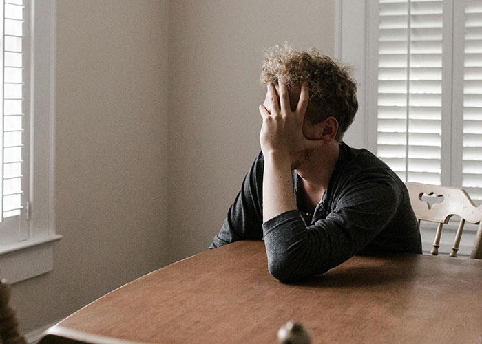 A man sits at a table, covering his face in distress, reflecting wedding exclusion. A man sits at a table, covering his face in distress, reflecting wedding exclusion.