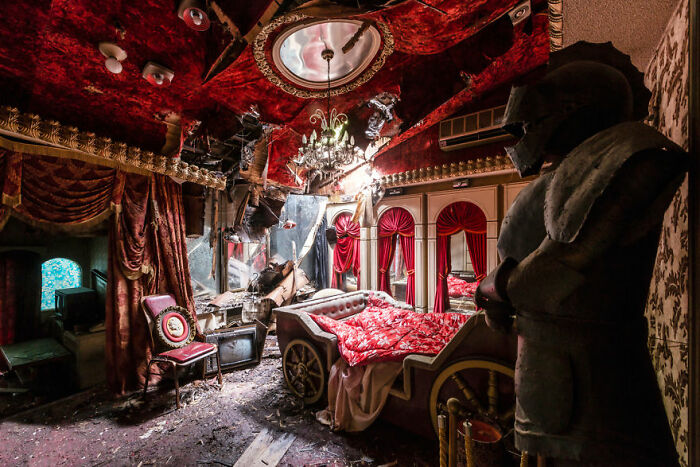 Eerie abandoned room with a carriage bed, red curtains, and a knight's armor.