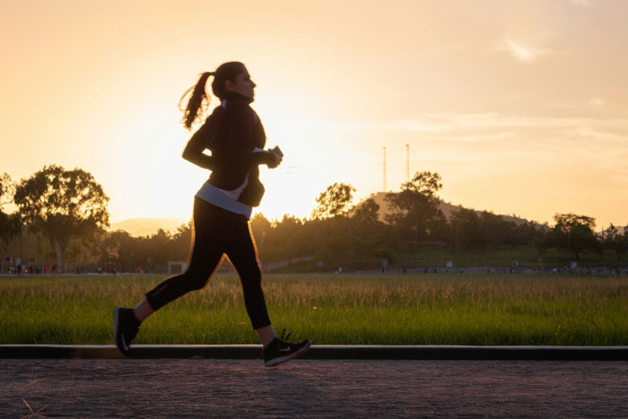 Woman running on a path at sunrise, engaging in a 5k run with trees and hills in the background. Woman running on a path at sunrise, engaging in a 5k run with trees and hills in the background.