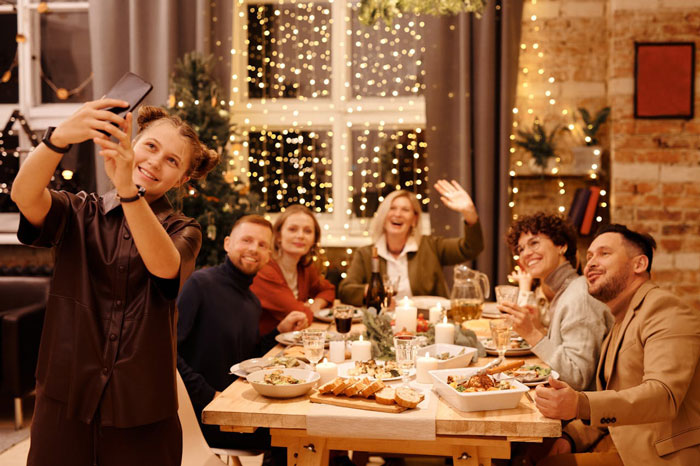 A woman takes a group selfie at a festive dinner with friends, capturing a joyful holiday moment. A woman takes a group selfie at a festive dinner with friends, capturing a joyful holiday moment.