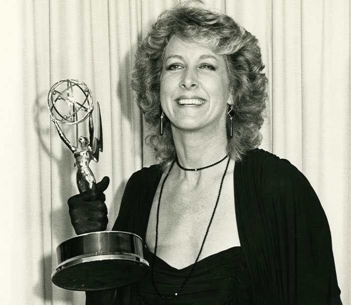 Smiling woman in black dress holding an award during a scandalous moment at an awards show.