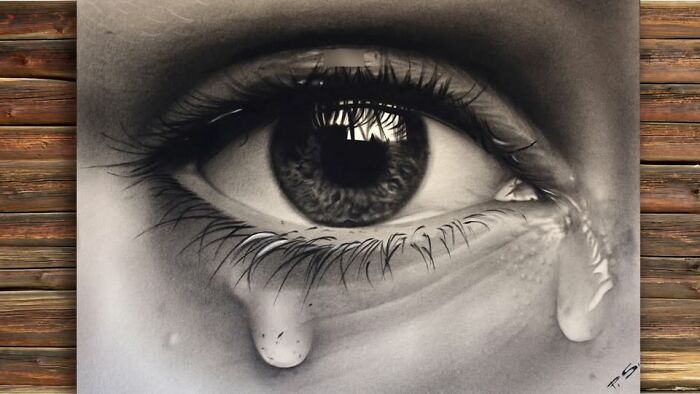 Hyper-realistic 3D drawing of a teary eye by German artist on wooden background.