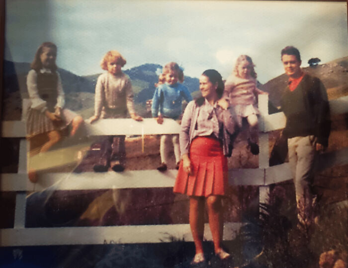 Vintage family photo showing candid glimpses into the past with children and adults outdoors by a white fence.
