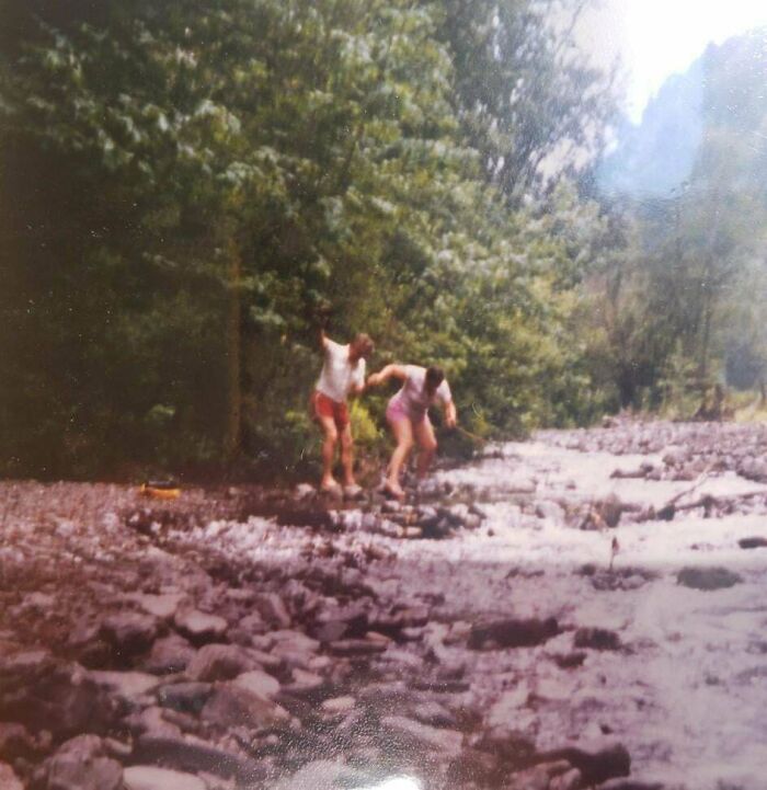 Two people balancing on rocks by a river in a candid glimpse into the past nature scene.