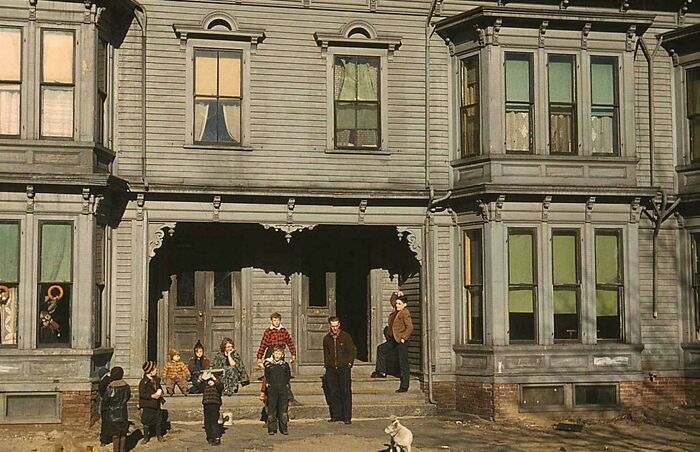 Group of children and a man in front of an old house, candid glimpses into the past with historical atmosphere.