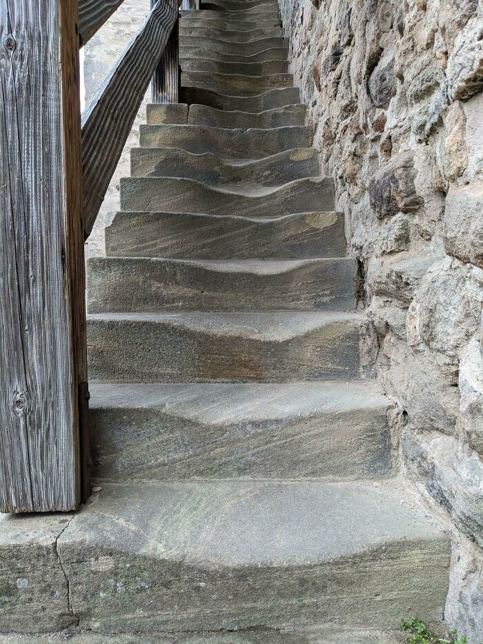 Worn stone steps showing the effects of time, bordered by a wooden railing and stone wall.