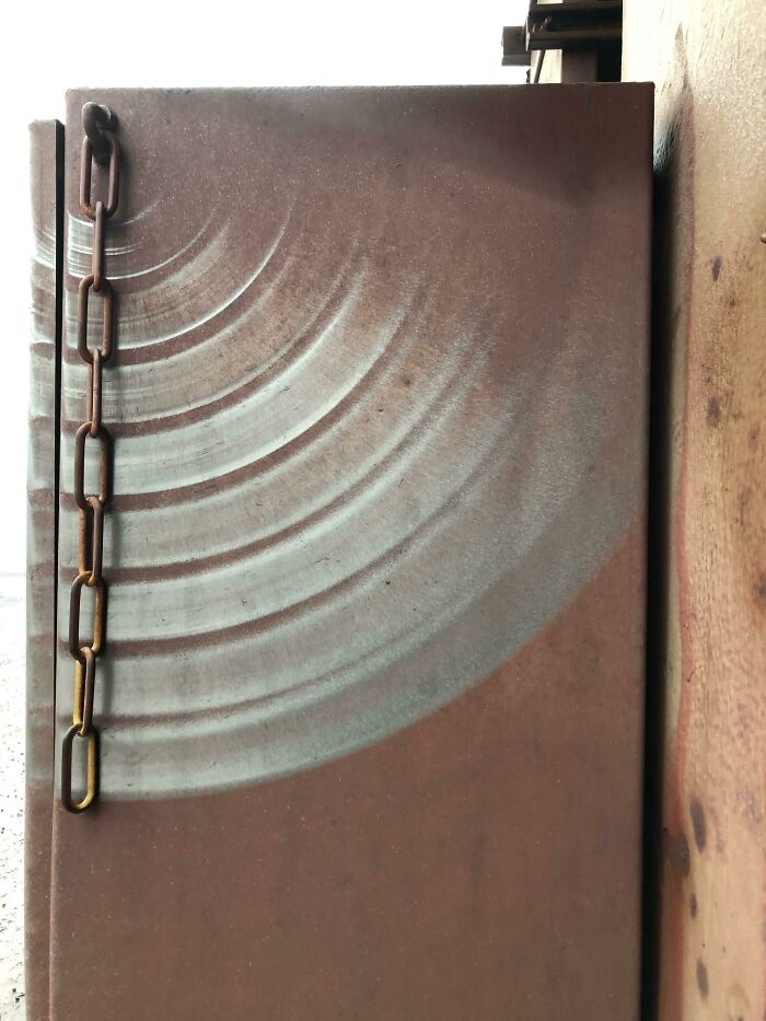 Rusty metal sheet with circular patterns and a hanging chain, illustrating the effects of time on things.