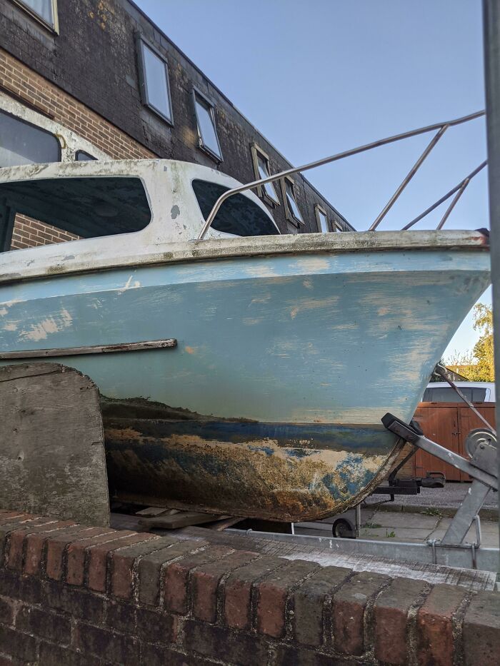 Old boat showing signs of wear, tied up on a trailer beside a brick wall, illustrating the effects of time vs. things.