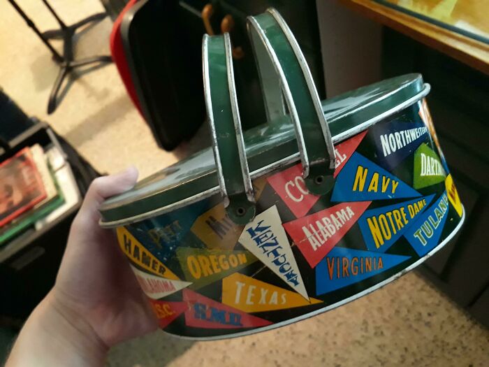 Hand holding a vintage tin with colorful pennant designs, representing various universities, highlighting things over time.