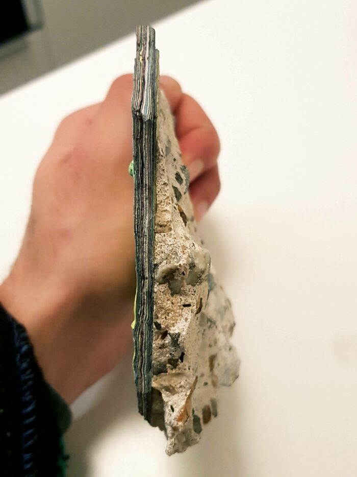 Close-up of a hand holding a slice of layered asphalt and rocks, illustrating Time-vs.-Things concept.