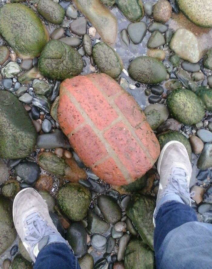 Feet standing on rocky beach, focusing on time-aged stone resembling a loaf of bread, showcasing time vs. things.