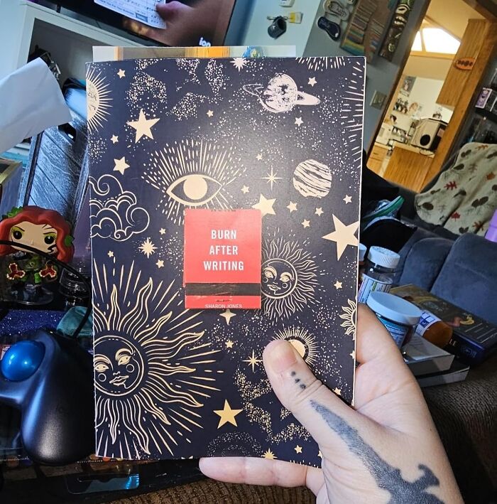 Person holding a "Burn After Writing" journal, suggesting digital detox through reflective writing in a cozy room.