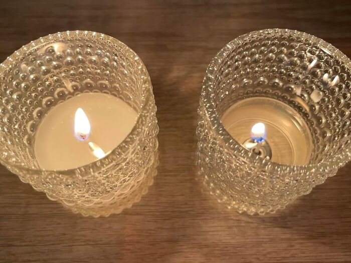 Two lit candles in textured glass holders on a wooden surface for a digital detox ambiance.